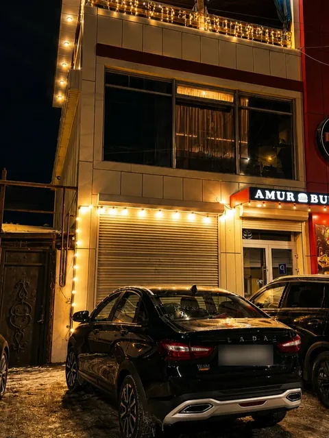 Вход в кафе ночью: гирлянды на фасаде, чёрная вывеска Amur Burger
